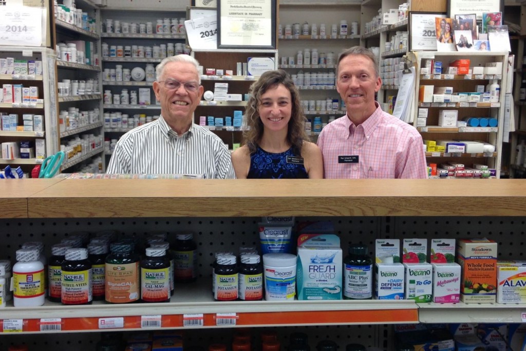 Ralph Ashworth, Cori, and Paul Ashworth stand behind the pharmacy counter at the drugstore